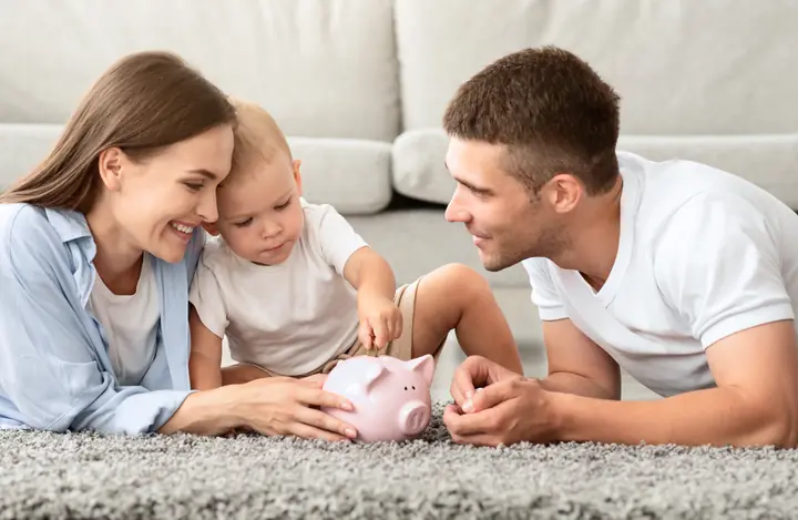 A family on the living room floor putting a coin in a piggy bank